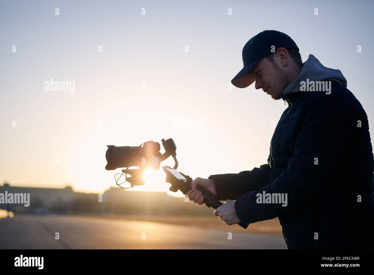 Junger Mann, der mit Kamera und Gimbal filmte. Videofilmer, der bei Sonnenaufgang gegen die Stadt steht. Prag, Tschechische Republik Stockfoto