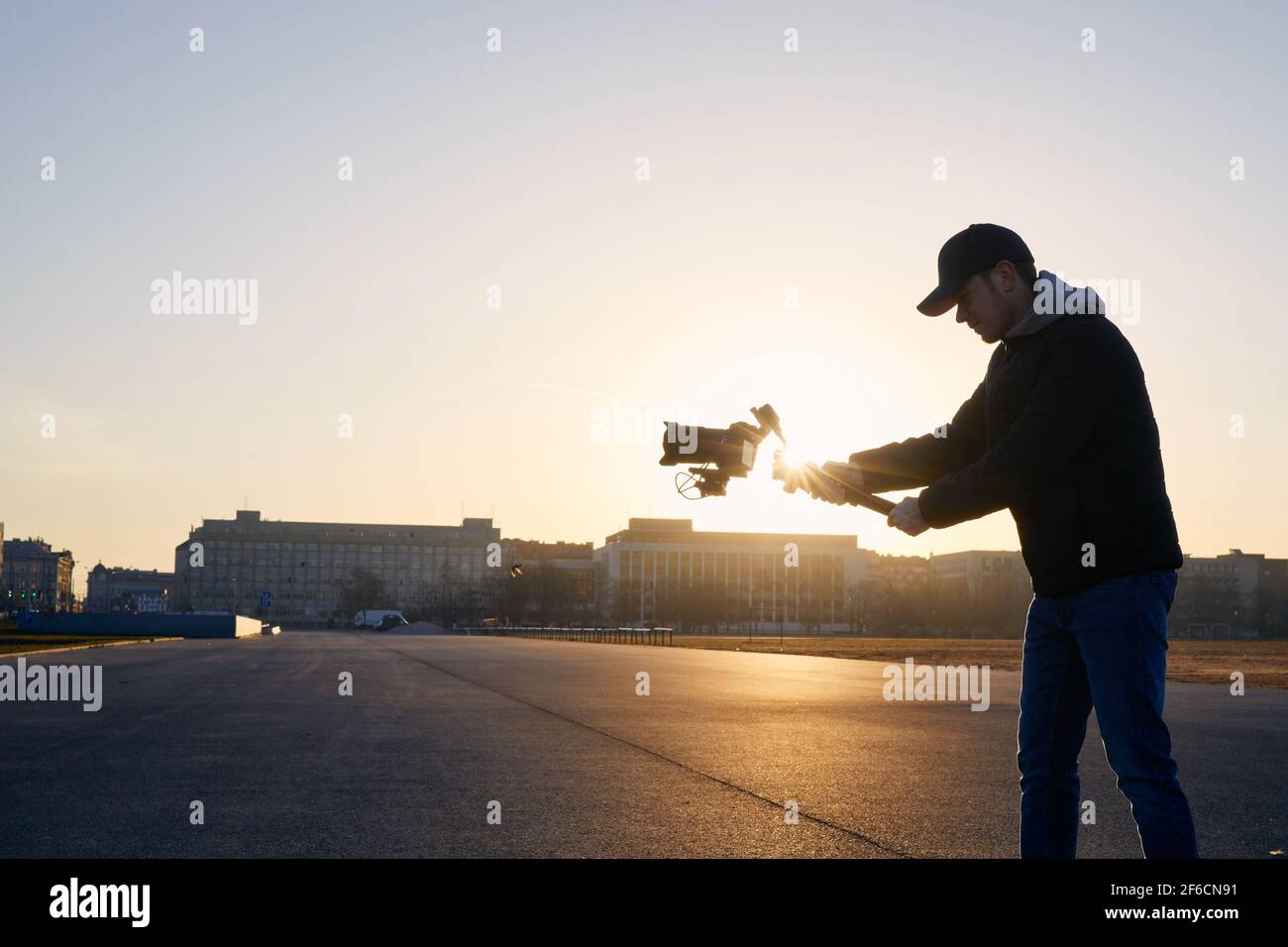Junger Mann, der mit Kamera und Gimbal filmte. Videofilmer, der bei Sonnenaufgang gegen die Stadt steht. Prag, Tschechische Republik Stockfoto