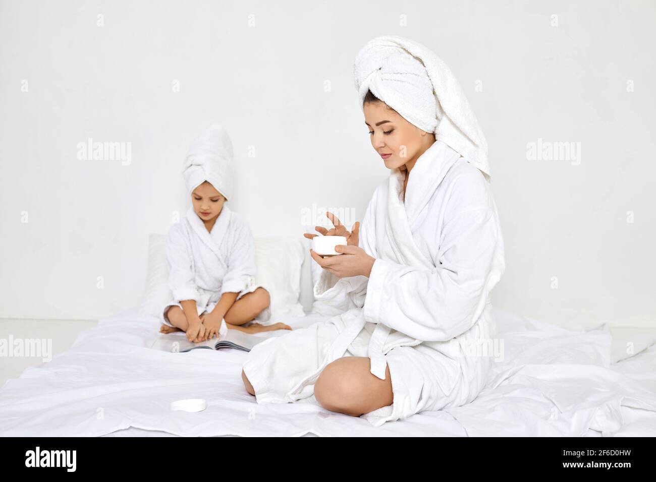 Mutter in weißen Bademänteln und Handtüchern Creme auf die Hände auftragen Stockfoto