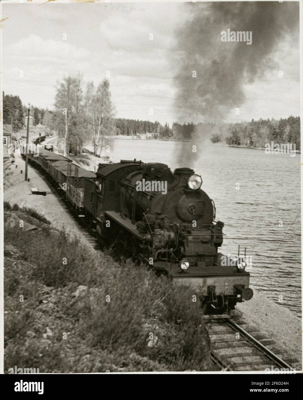 Die Verkehrsgesellschaft Grängesberg - Oxelösund Eisenbahn, TGOJ M3T 73 vor einer Reihe von Erzautos in Harsjön. Stockfoto