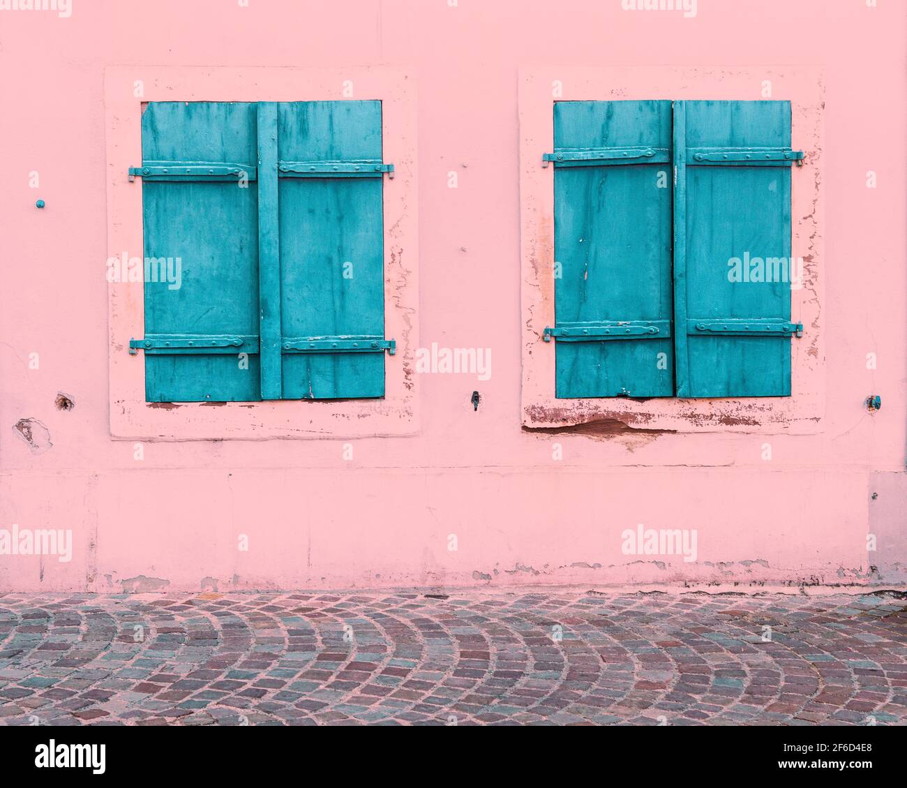 Zwei Fenster mit geschlossenen blauen hölzernen Fensterläden auf einem alten Haus mit einer weißen Wand Stockfoto