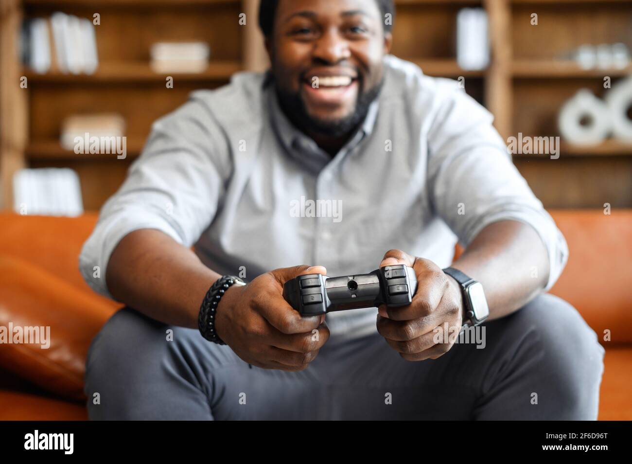 Fokus auf Joystick für Videospiele, schwarz aufgeregt Mann aus Fokus, sitzen auf Ledersofa, halten Joystick spielen Videospiele, entspannen an einem Wochenende, eine Pause von der Arbeit, allein zu Hause leben Stockfoto