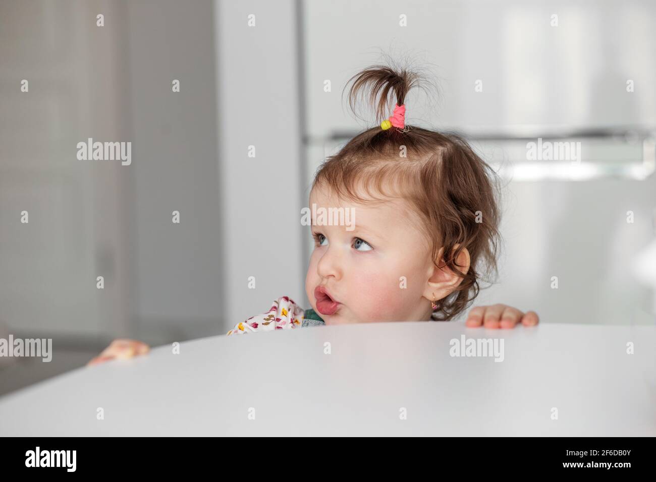 Ein kleines Mädchen in der Küche starrt von der Kamera weg. Stockfoto