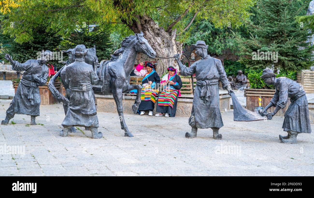 Shangrila China , 10. Oktober 2020 : zwei Frauen in traditioneller Kleidung in der Mitte von Statuen in der Straße der Dukezong Altstadt Shangri-La Yunnan China Stockfoto