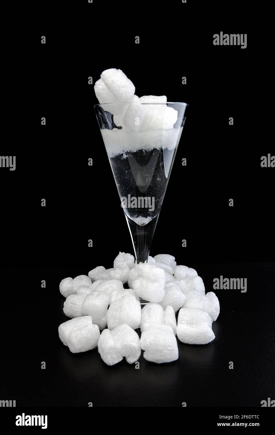 Biologisch abbaubare, schützende lose Fill-Chips aus Stärke lösen sich in einem Weinglas mit Wasser auf. Stockfoto