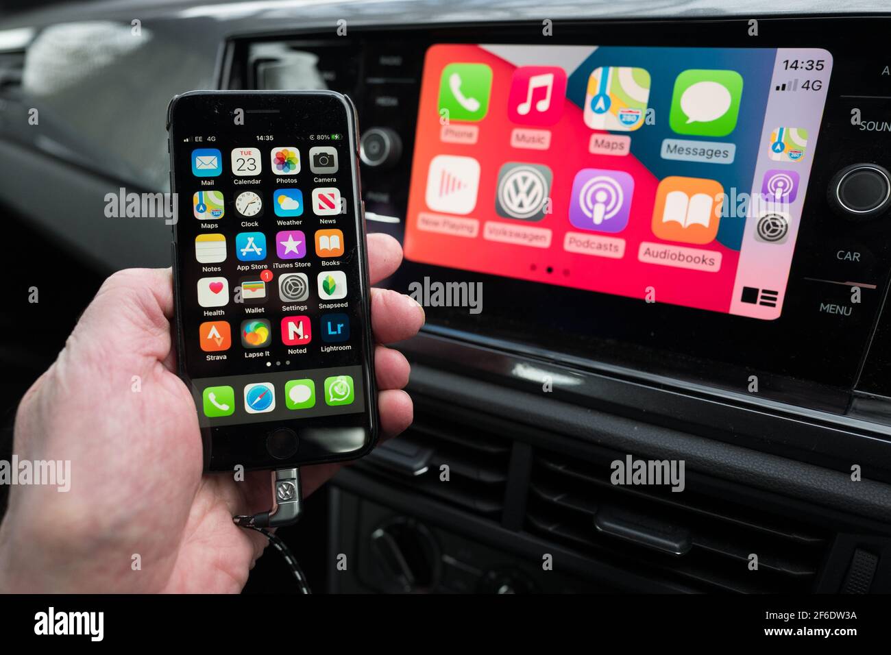 Mann, der sein Apple iphone benutzt, verbindet auch die Unterhaltungs- und Kommunikationseinheit im Auto in einem VW Polo. Stockfoto