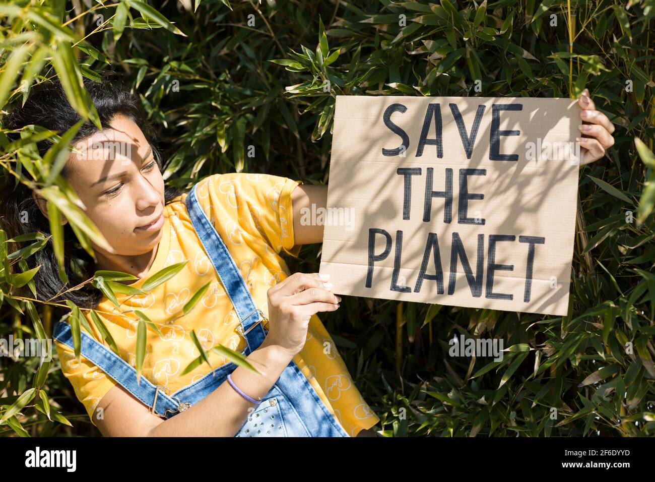 Porträt einer jungen Frau in der Natur mit einem Banner mit dem Text Save the Planet. Sie ist draußen. Stockfoto