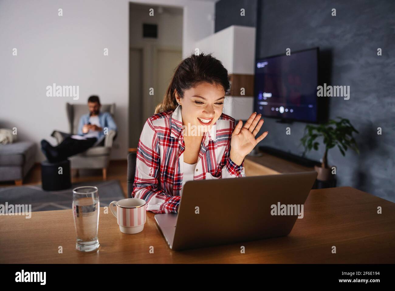 Lächelnde glückliche Frau, die zu Hause während der Sperre sitzt und Videoanruf mit ihren Lieben hat. Stockfoto