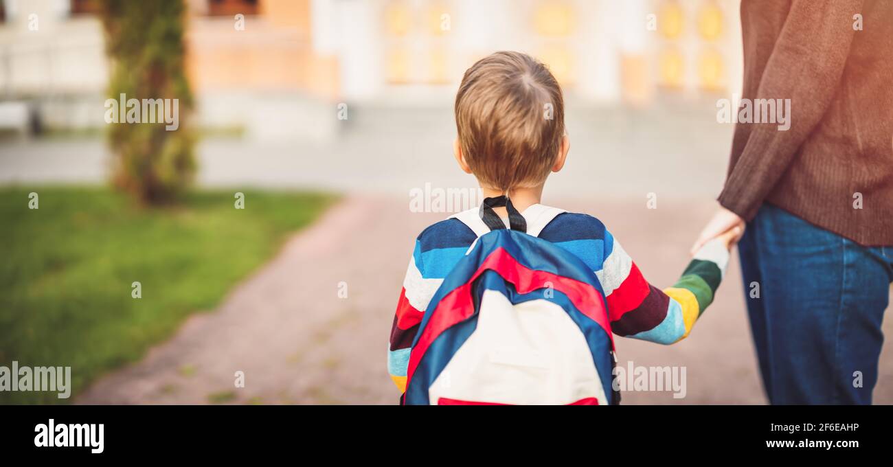 Kind mit Rucksack und mit Mutter vor einem Schulgebäude Stockfoto