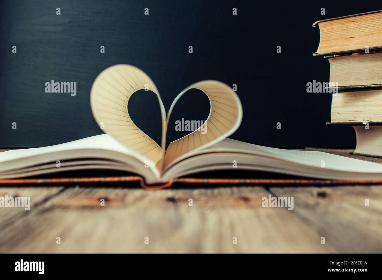 Blätter eines Notebook in einem Käfig in der Form eines Herzens gewickelt. Im Hintergrund ist ein Stapel von Büchern und einem schwarzen Brett. Bildung Konzept. Valentine's D Stockfoto