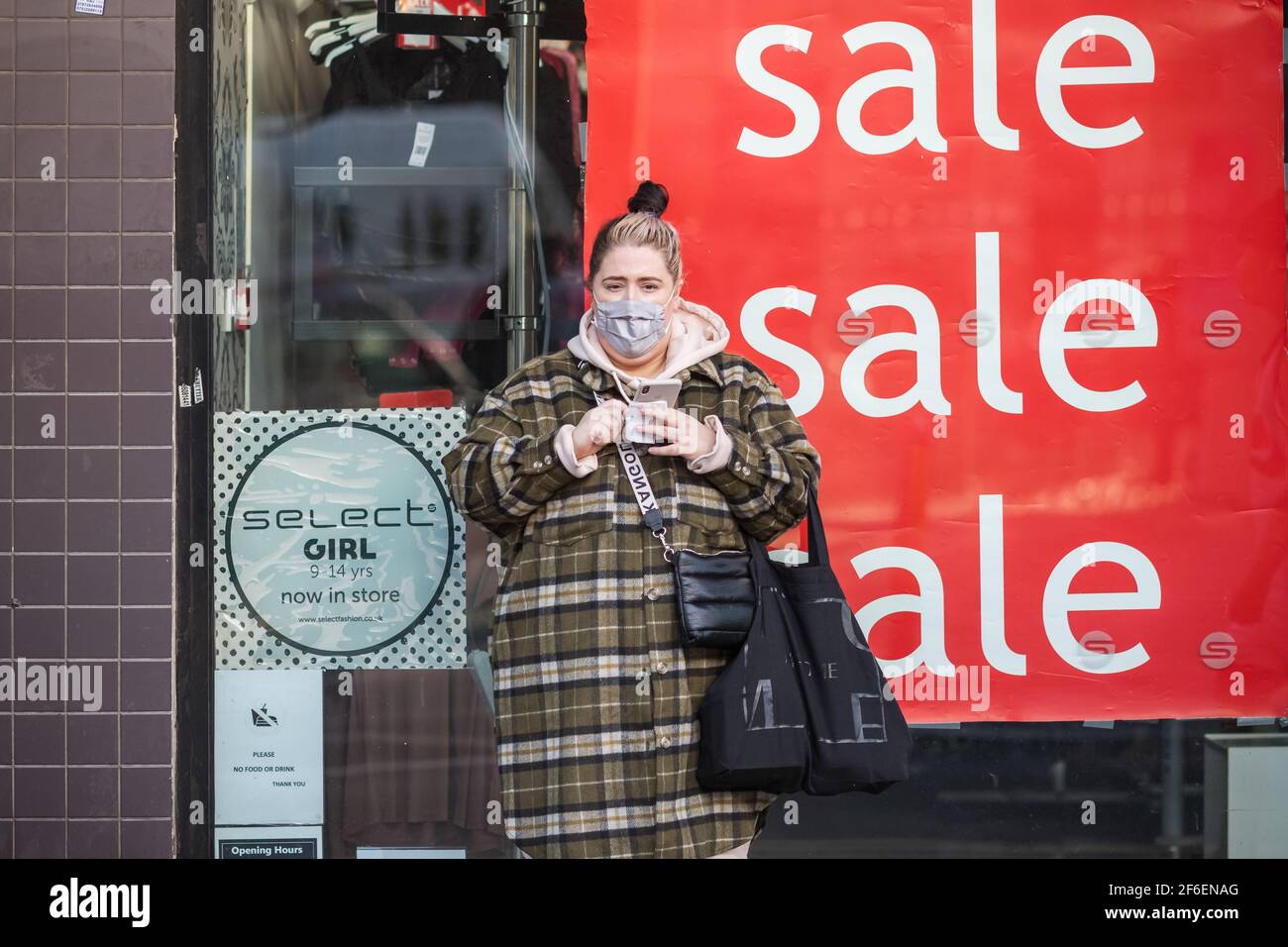 London, UK - 5 Februar, 2021 - EINE weibliche Shopper mit einer schützenden Gesichtsmaske und Verkaufsschilder in einem Geschäft auf Wood Green High Street angezeigt Stockfoto