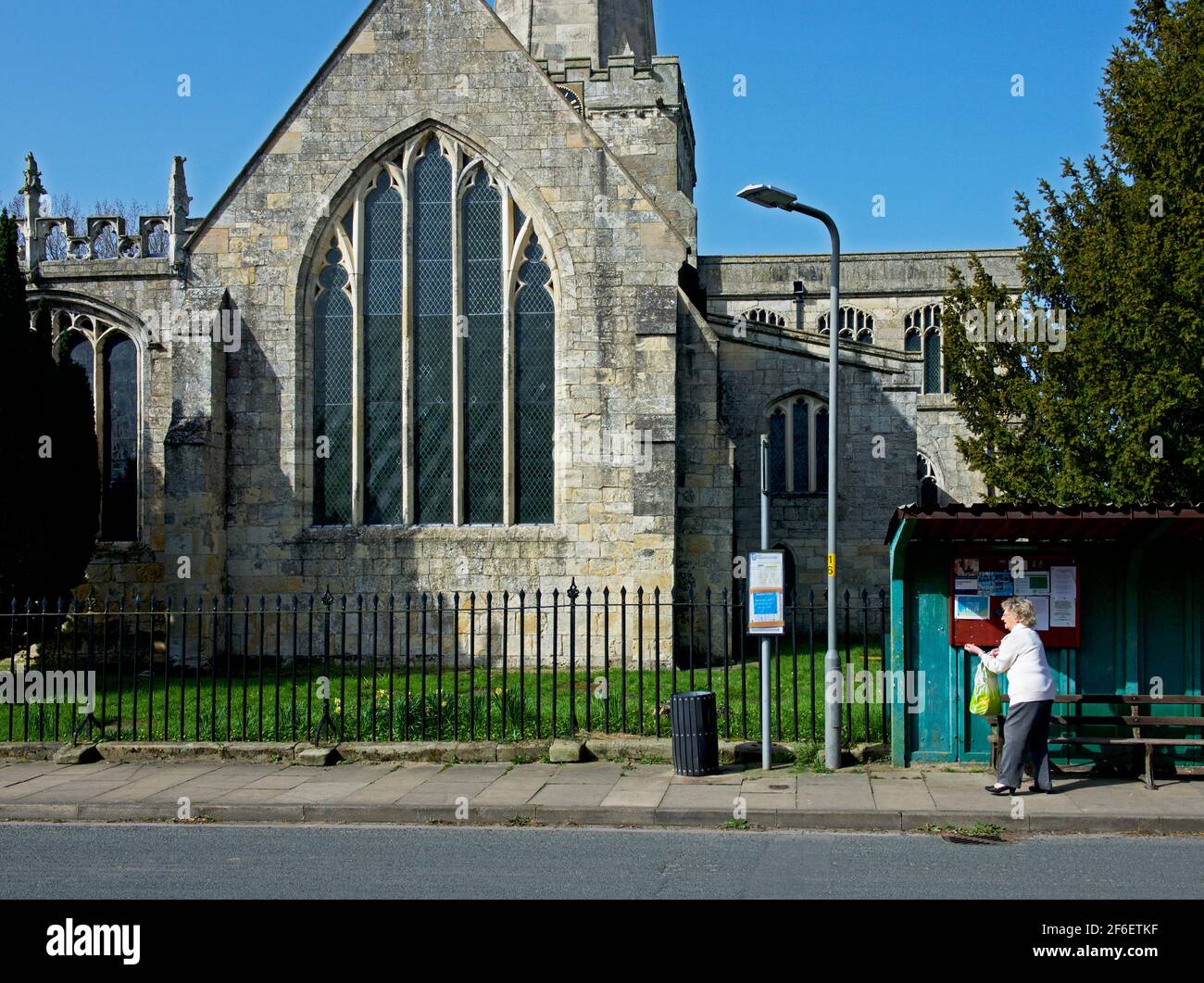 Die elderley-Frau wartet an der Bushaltestelle vor der Kirche im Dorf Hemingbrough, East Yorkshire, England Stockfoto