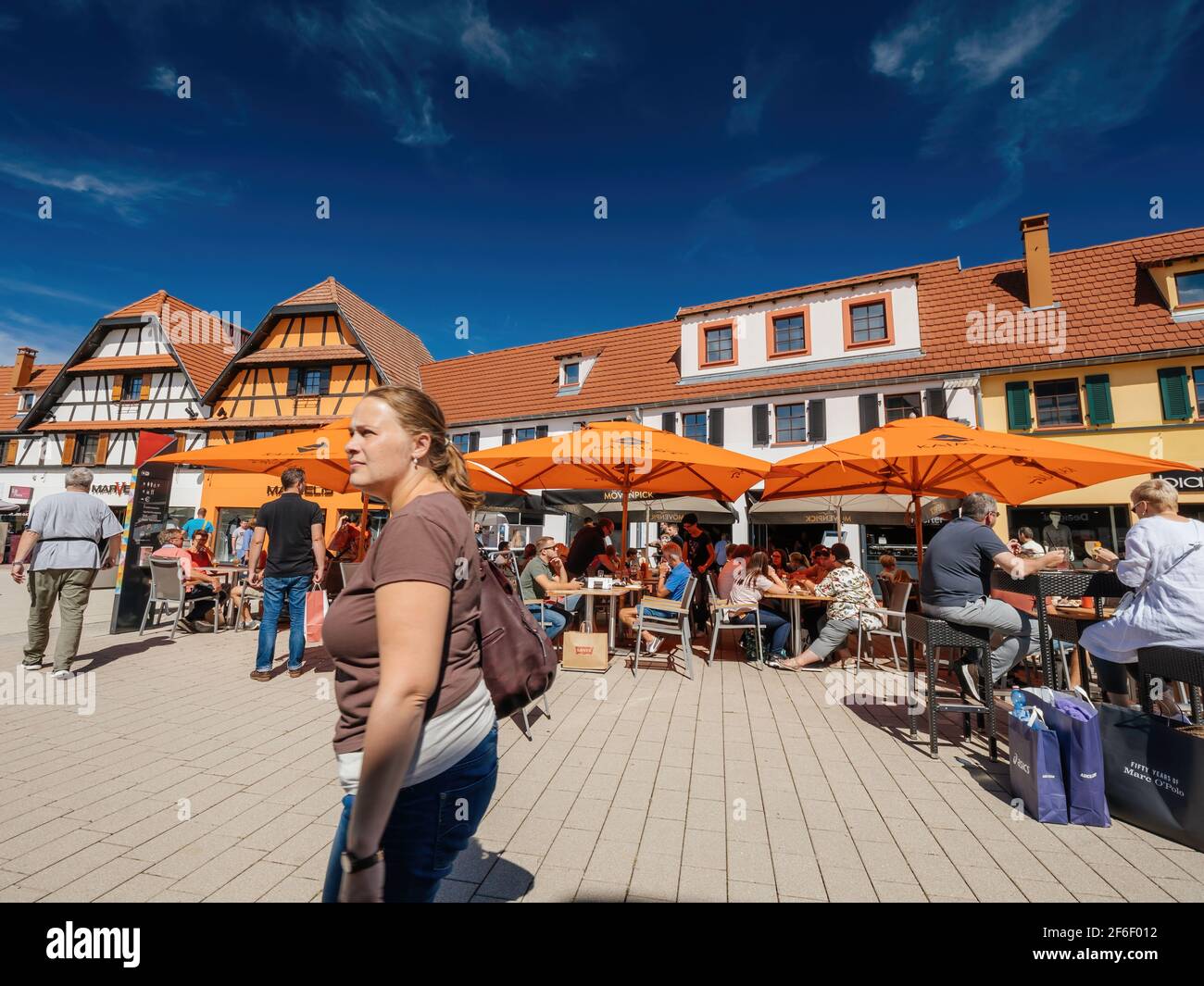 Junge Frau zu Fuß mit Terrasse im Hintergrund bei mehreren Geschäfte im Roppenheim The Style Outlet Stockfoto