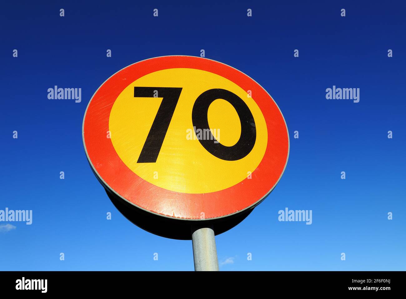 Low-Angle-Ansicht des kreisförmigen gelben 70 Geschwindigkeitsbegrenzungsfahrbahnschildes mit einer roten Grenze gegen einen blauen Himmel. Stockfoto