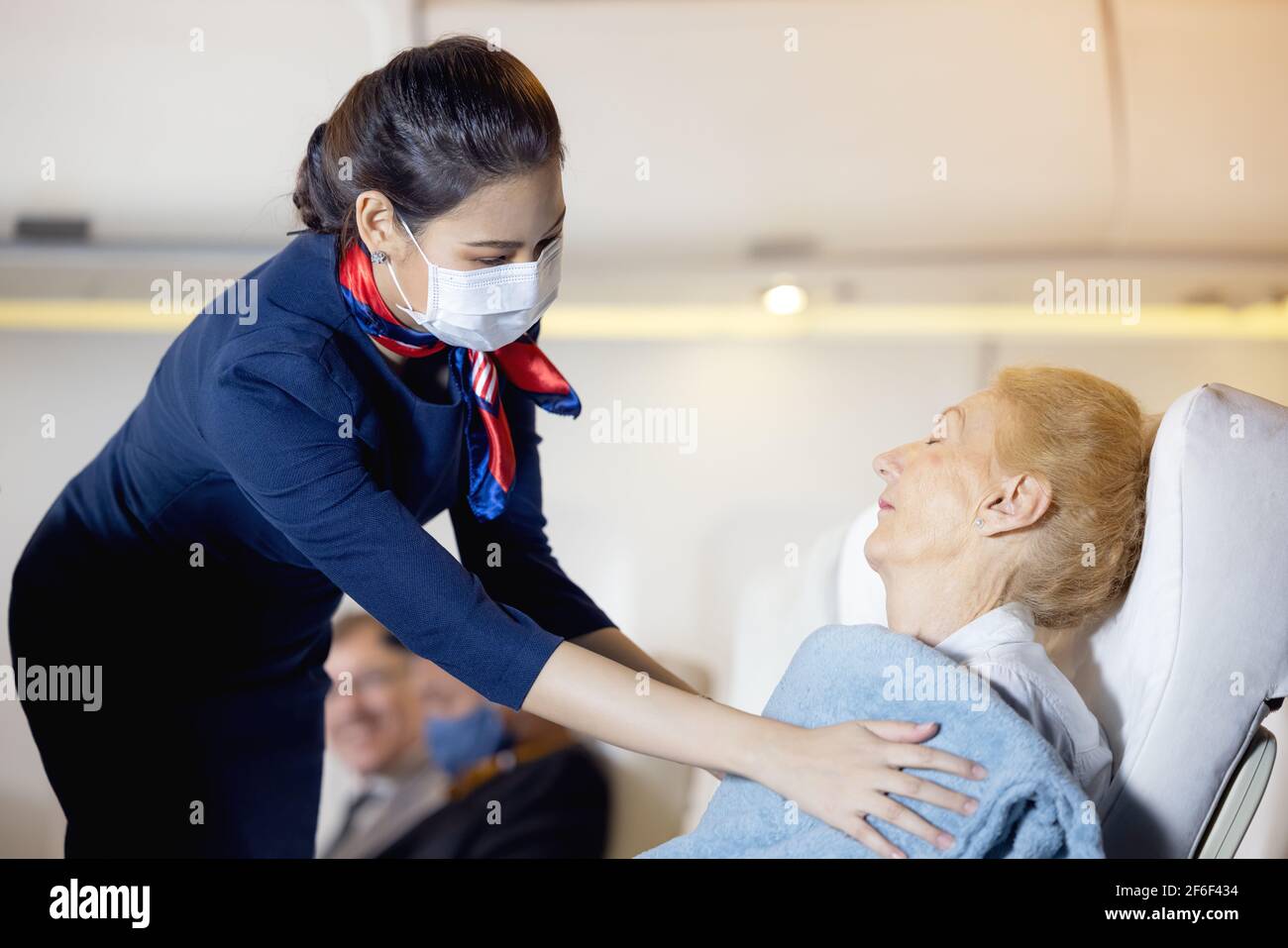 Eine Flugbegleiterin bekleidete einen älteren Passagier, der auf dem Beifahrersitz schlief. Stewardess, die sich um den Passagier kümmert. Das Kabinenpersonal gibt es Stockfoto