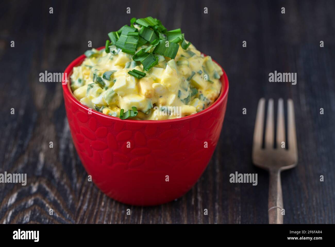 Gesunder Salat aus grünem Wildlech, pochiertem Ei und saurer Creme in roter Schüssel, Nahaufnahme. Salat mit wildem Knoblauch und gekochten Eiern Stockfoto
