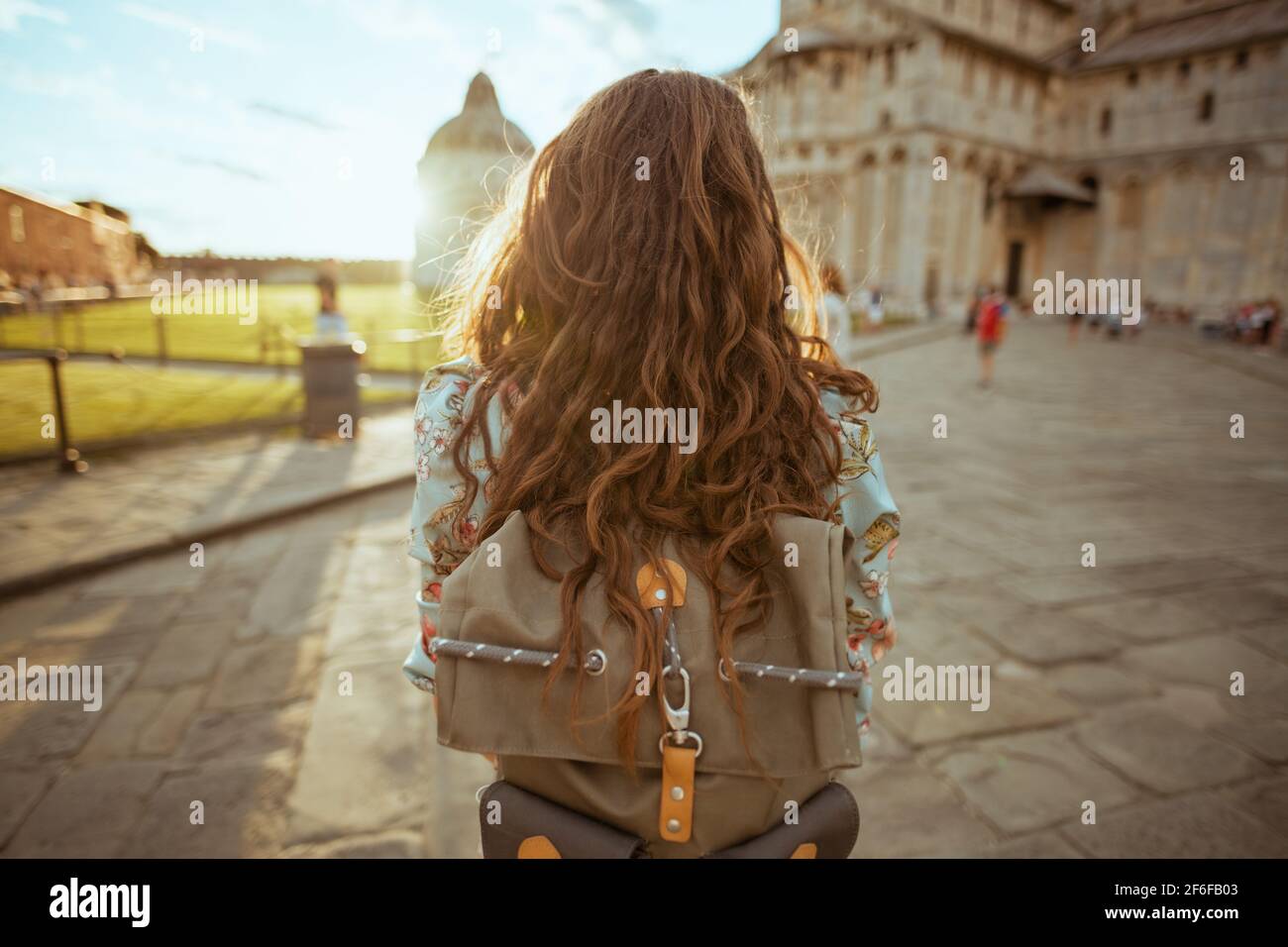 Von hinten gesehen moderne Frau in Blumenkleid mit Rucksack mit Rundgang in der Nähe Cattedrale di Pisa. Stockfoto