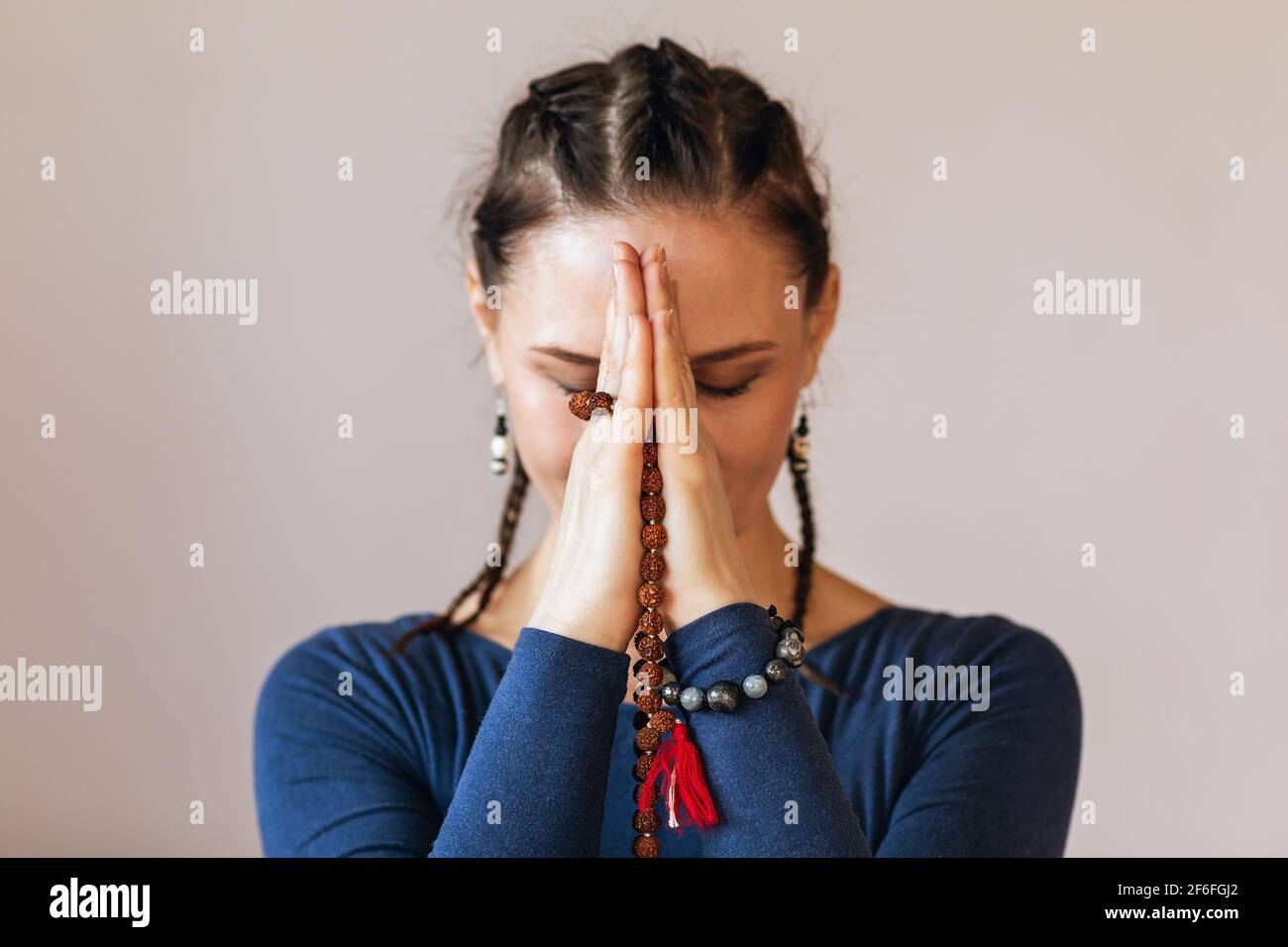 Eine Frau, die Yoga praktiziert, meditiert mit Namaste in der Nähe ihres Gesichts, hält einen Rosenkranz in den Händen, aus der Nähe. Stockfoto