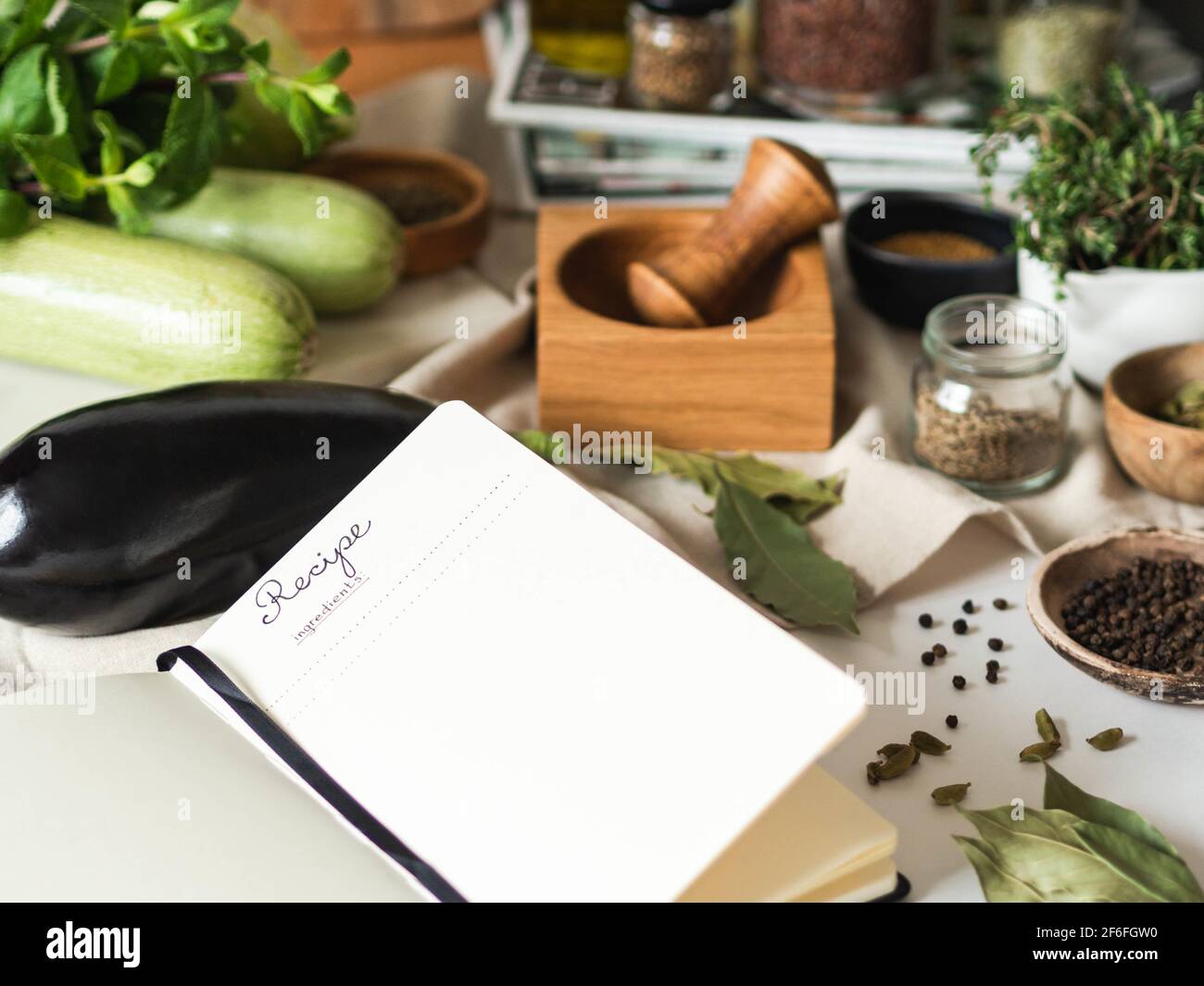 Offenes Notizbuch für Kochrezepte und verschiedene vegetarische Zutaten auf dem Küchentisch. Vorderansicht Stockfoto