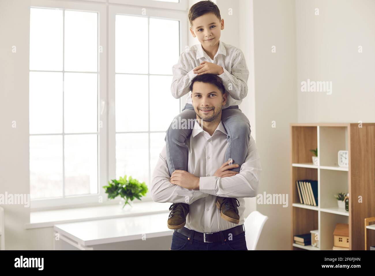 Lächelnder kaukasischer Vater hält den Sohn auf den Schultern und schaut beide an Kamera im Hochformat Stockfoto