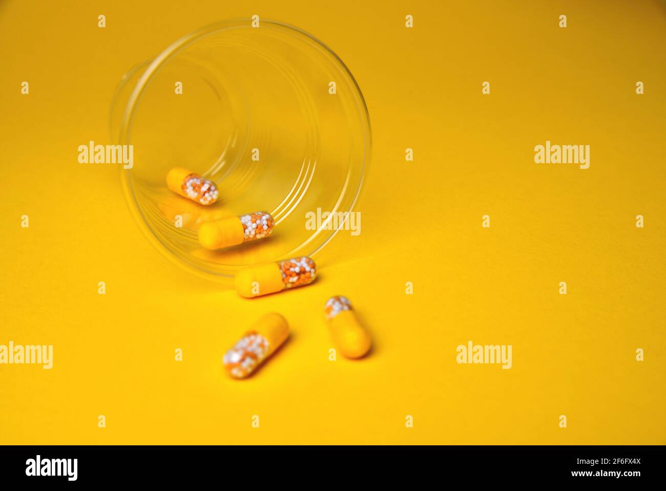 Kapseln in einem Glasbecher. Medizinische Tabletten, Vitamine in einem Granulat, in gelben Kapseln auf einem gelben Hintergrund. Blur als kreative Idee des Autors, Stockfoto