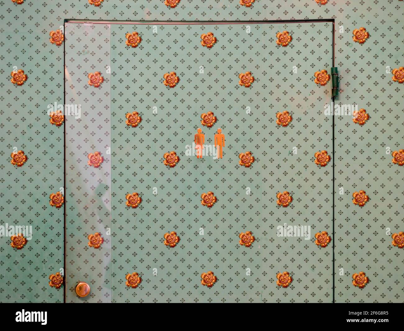 Versteckter Toiletteneingang: Die Tür für eine Unisex-Toilette versteckt hinter Vintage-Tapeten in diesem ehrwürdigen Museum. Farblich abgestimmte Aufkleber kennzeichnen die Tür diskret. Stockfoto