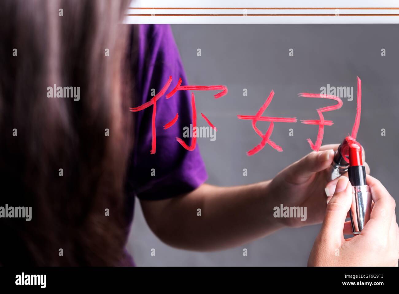 Nahaufnahme einer weiblichen Person, die einen chinesischen Gruß schreibt Wort auf einem Spiegel mit einem roten Lippenstift Stockfoto
