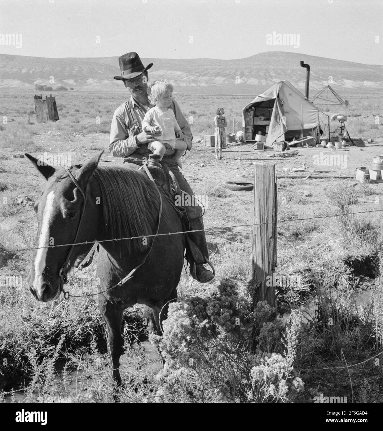Herr Fairbanks und sein Kind zu Pferd mit seiner Frau und ihrem Zelt im Hintergrund. Die Familie Fairbanks ist innerhalb eines Jahres an drei verschiedene Orte des Projekts gezogen. Willow Creek Area, Malheur County, Oregon. 1939. Foto von Dorothea lange. Stockfoto