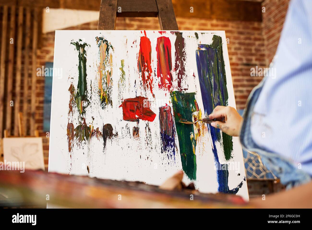 Maler im Atelier, der mit Ölgemälden und Palettenmesser abstrakte Bilder auf Leinwand schafft. Junge Künstlerin arbeitet. Kreativer Prozess, entspannen Stockfoto