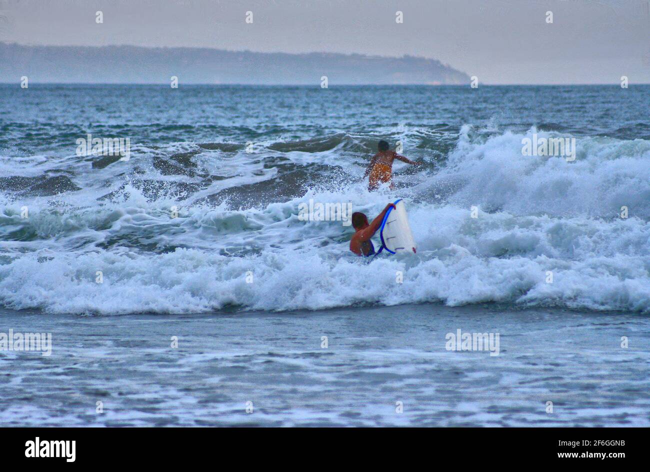 Zwei Surfer in den Wellen vor Bali, Indonesien, am späten Nachmittag an einem bewölkten Tag. Stockfoto