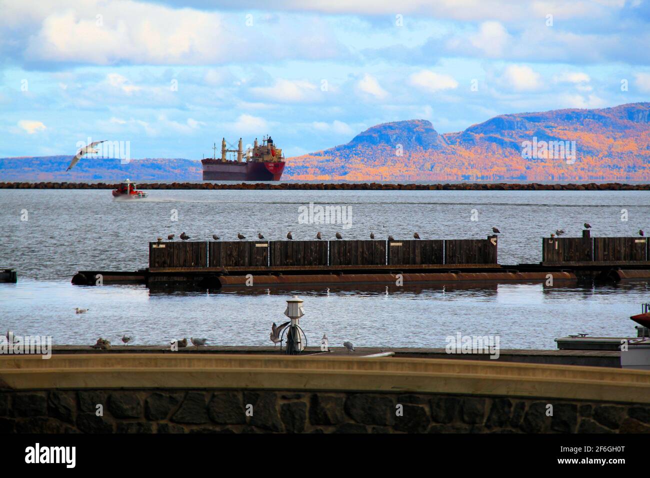 Holzstrukturen liegen vor dem Foto des Lake Superior, während ein Ozeanfrachter hinter der Bruchmauer wartet, bis er sich mit Getreide beladen hat. Stockfoto
