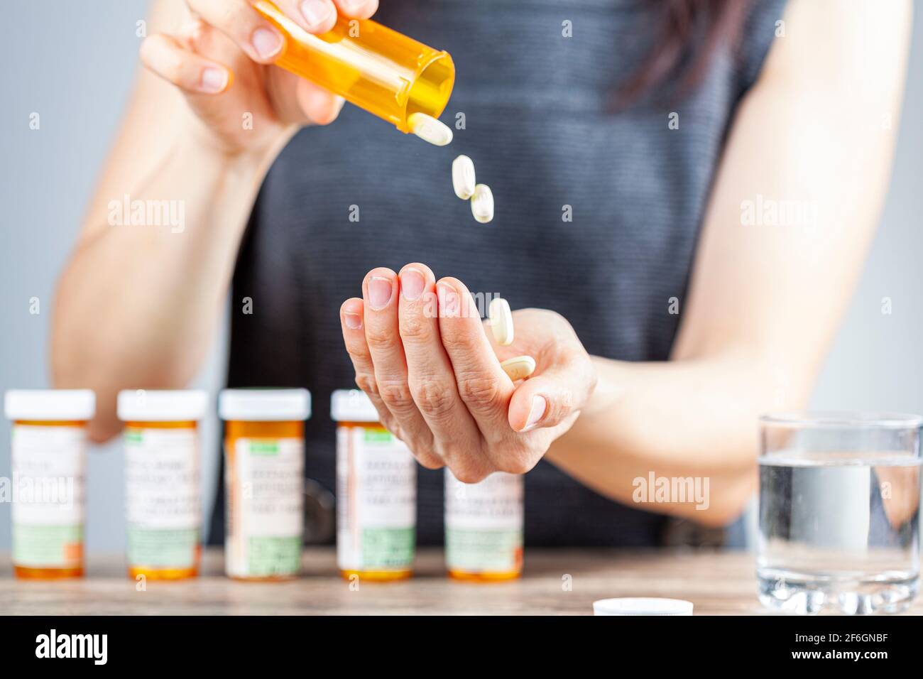 Eine junge depressive Frau nimmt Pillen aus der Medikamentenflasche. Sie hat einen Stapel Flaschen auf der Rückseite aufgereiht. Konzeptbild für Drogenkonsum, Ove Stockfoto