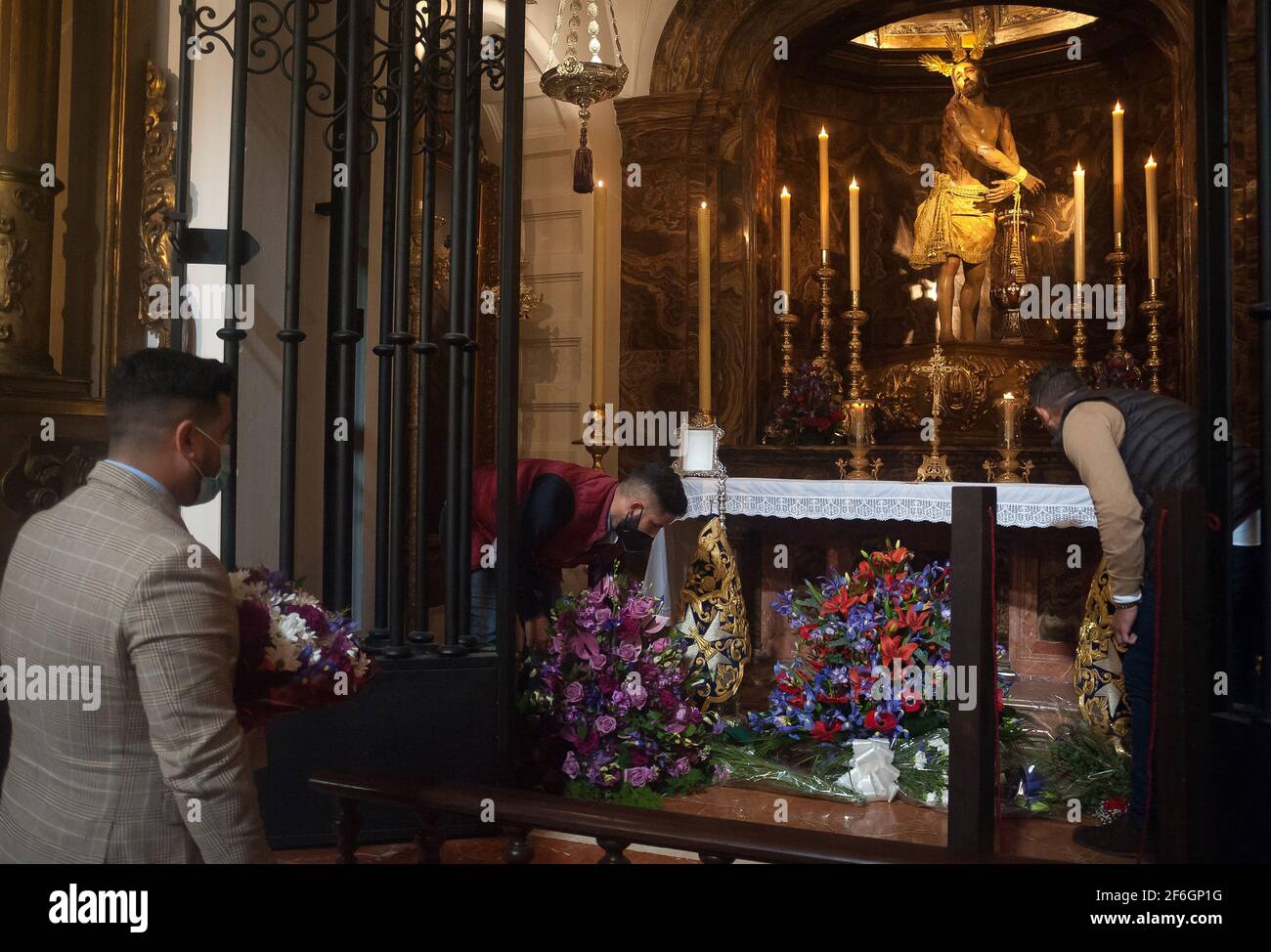 Gläubige platzieren Blumensträuße an einer Figur Christi in der Kirche von Santiago, als Teil der Verehrung während der Karwoche. Trotz der Absage der Karwoche Prozessionen haben viele Bruderschaften beschlossen, Messen zu organisieren, Verehrung und Ausstellung von Figuren von Christus und der Jungfrau heiraten mit in Kirchen nach allen Schutzmaßnahmen gegen Covid19. Stockfoto