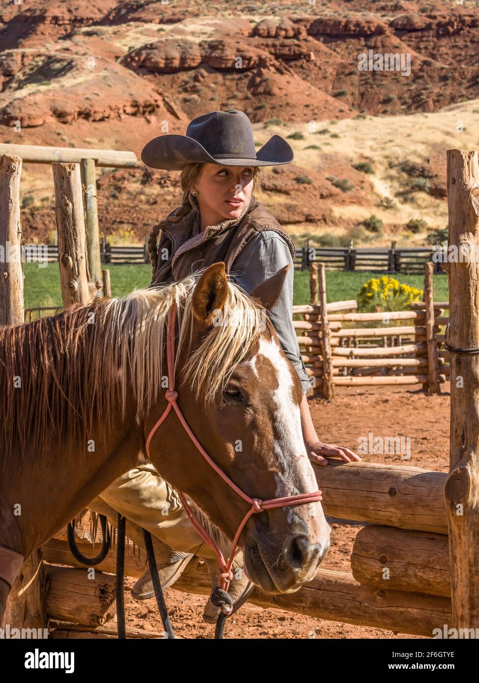Eine junge attraktive Arbeitsbedingungen cowgirl Wrangler sitzt auf einem Holz Schiene Zaun von Ihrem Pferd auf einer Ranch in der Nähe von Moab, Utah. Stockfoto