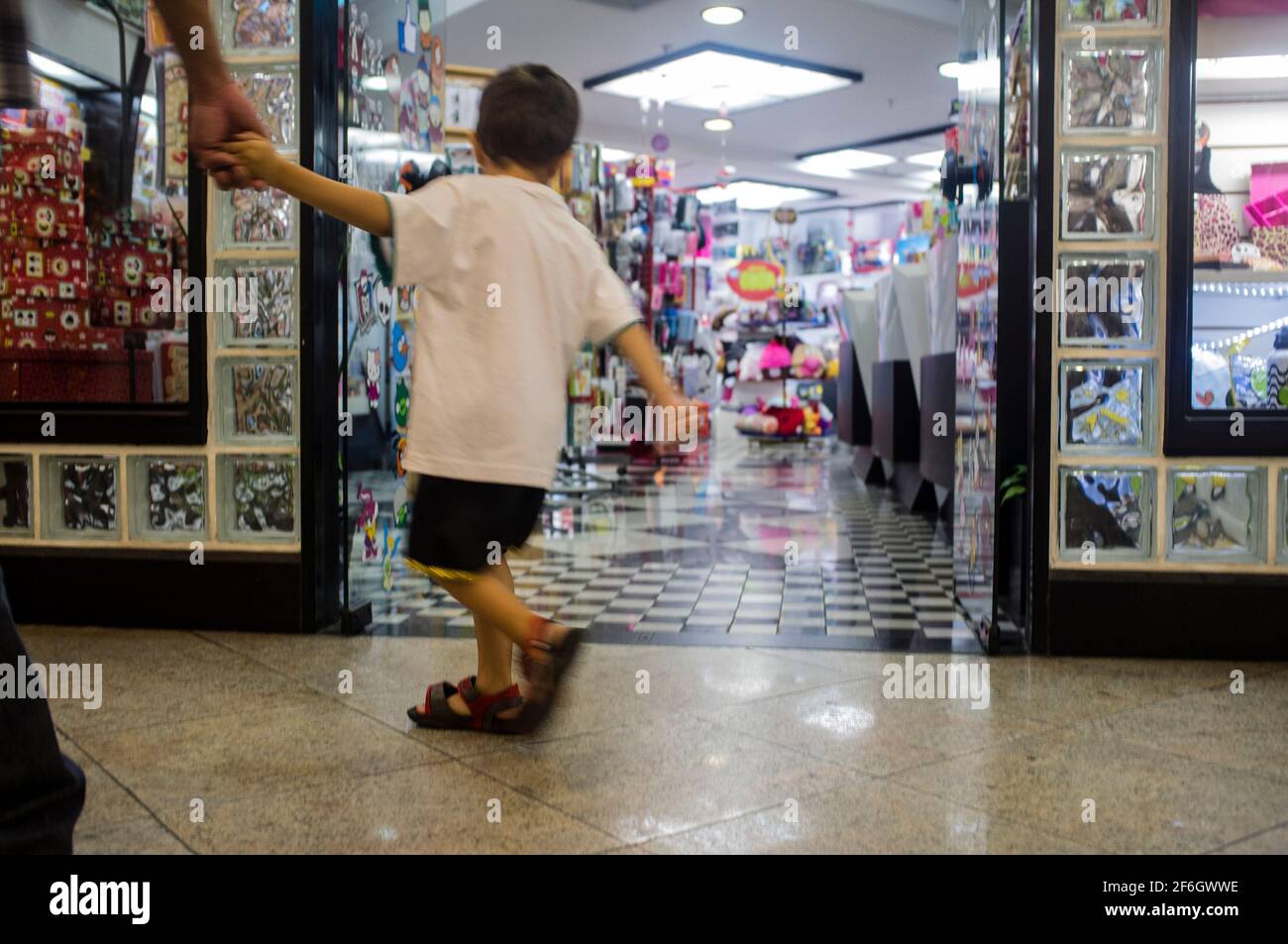Der 6-jährige Junge versucht, in Schreibwaren zu kommen, während seine Mutter seine Hand hält und ihn herauszieht, in einem Einkaufszentrum in Nova Friburgo, Bundesstaat Rio de Janeiro, Brasilien. Stockfoto