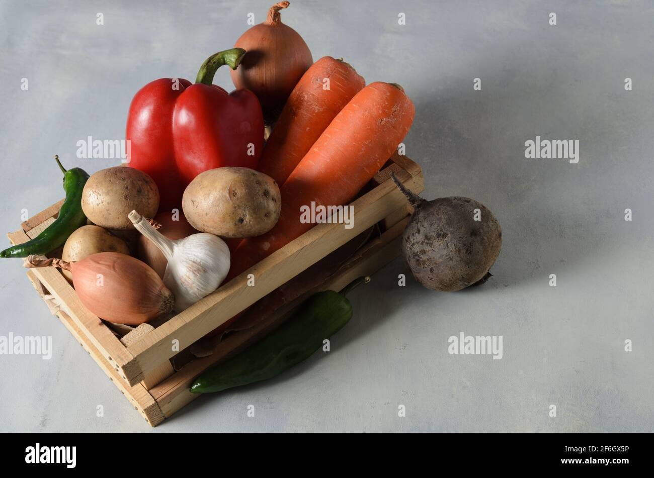 Gemüse in einer Holzkiste. Set aus Gemüse, Kartoffeln, Zwiebeln, Knoblauch, Pfeffer, Rüben zum Kochen Borscht auf einem strukturierten gelb-grauen Hintergrund. Auswahl Stockfoto