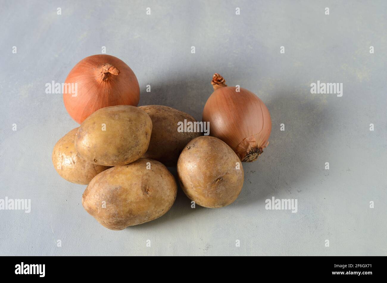 Kartoffelknollen mit Zwiebeln und Knoblauch auf einem strukturierten gelb-grauen Hintergrund. Selektiver Fokus. Stockfoto