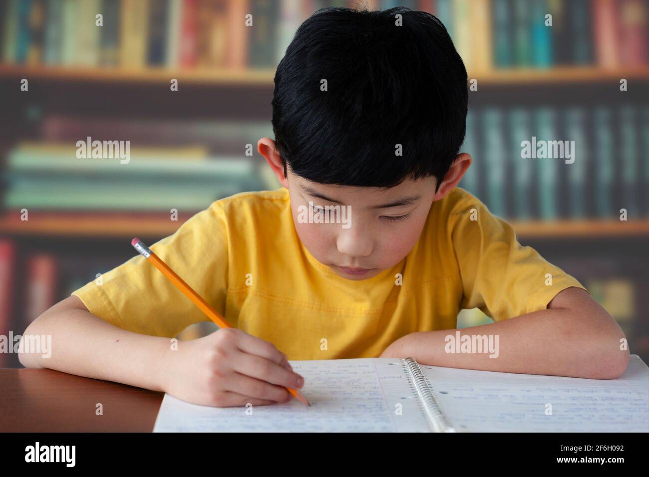 Junger asiatischer Junge, der in einer Bibliothek studiert und Hausaufgaben macht. Stockfoto