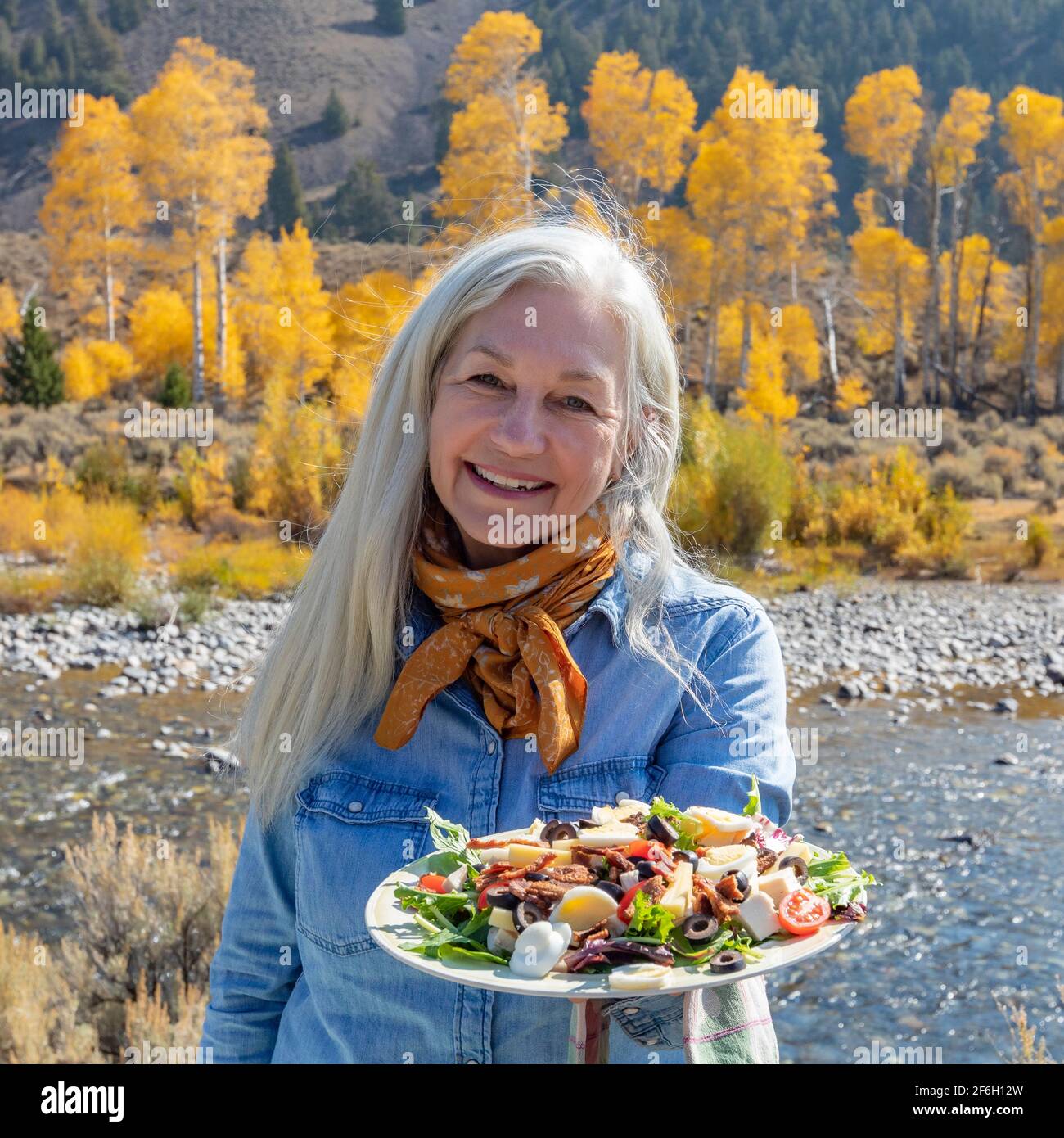 USA, Idaho, Sun Valley, Außenportrait einer älteren Frau, die im Herbst am Fluss entlang einen Salat hält Stockfoto