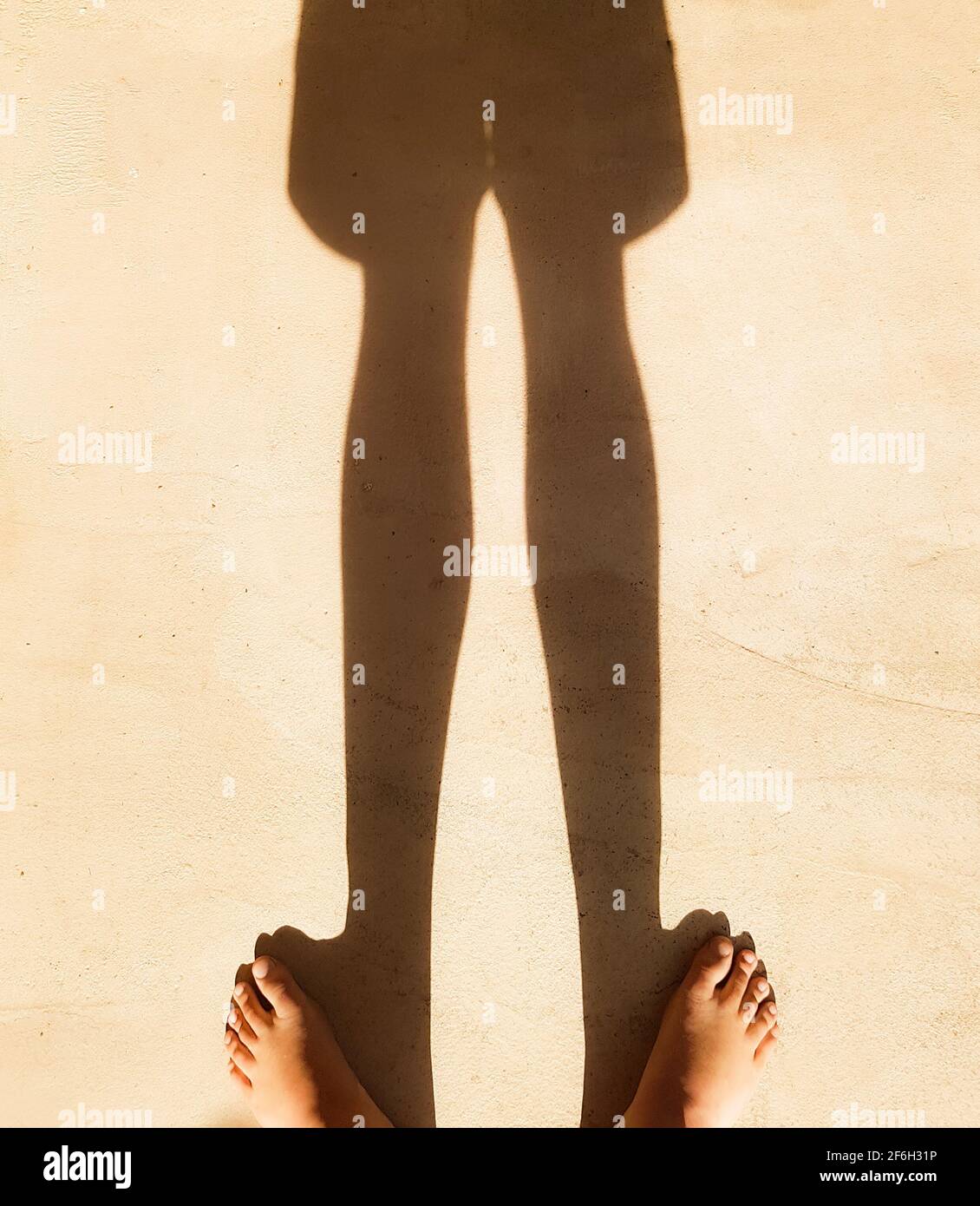 Junge steht barfuß steht in Sonnenschein Schatten auf dem Boden Beine und Shorts beobachten Zehen Fuß Füße Kind Kindheit Silhouette, barfuß gehen, Freiheit Stockfoto