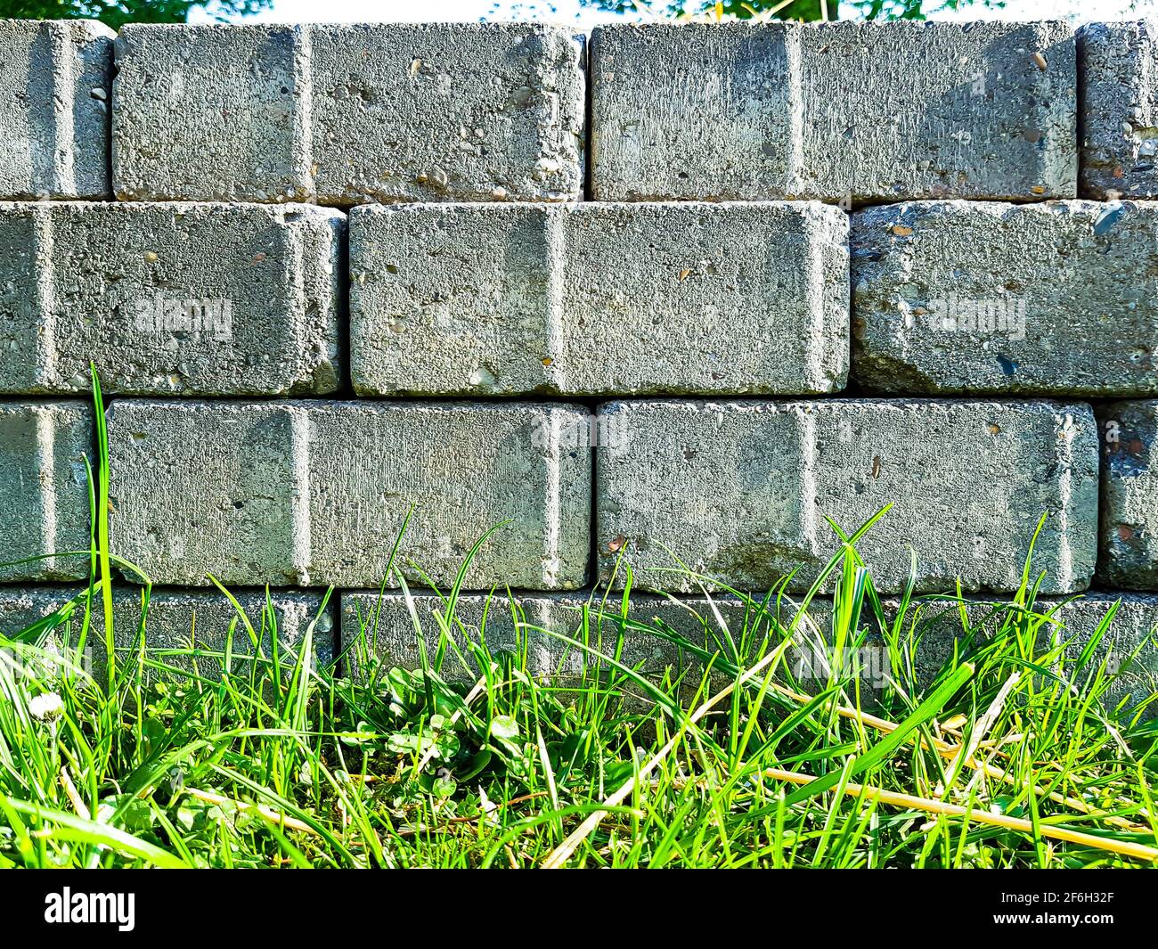 Trockene Steinmauer Ziegel Pflaster Steine Beton grau gestapelt Mauerwerk Grenze, Zaun Grenze Gras Sonnenbank Grenze Hintergrund alte Architektur verwittert Stockfoto