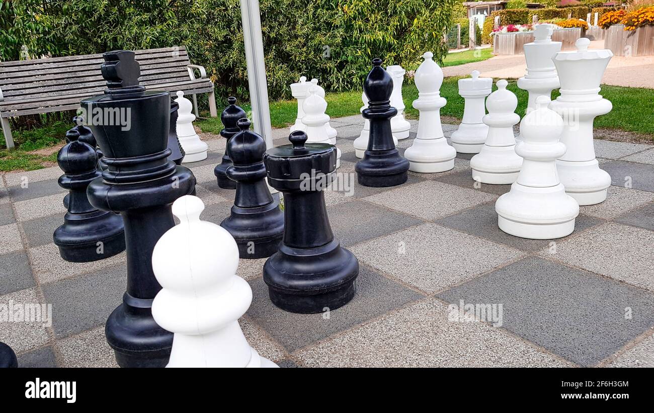 Schachspiel im Park draußen im grünen Riesen Feld Bereich Boden Schachfiguren schwarz weiß Erholung Hobby Turnier Freizeit Strategie Sommer Stockfoto