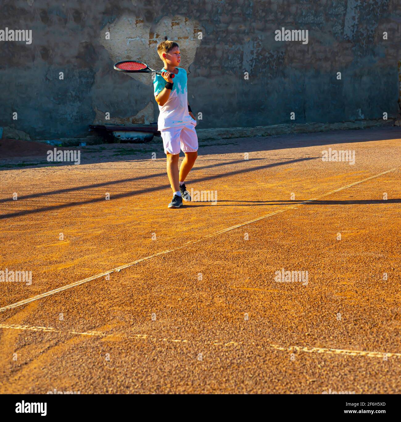 Junger Teenager-Tennisspieler auf einem Sandplatz. Es ist ein Herz an der Wand. Professionelles Tennistraining. Liebe zum Sport. Stockfoto