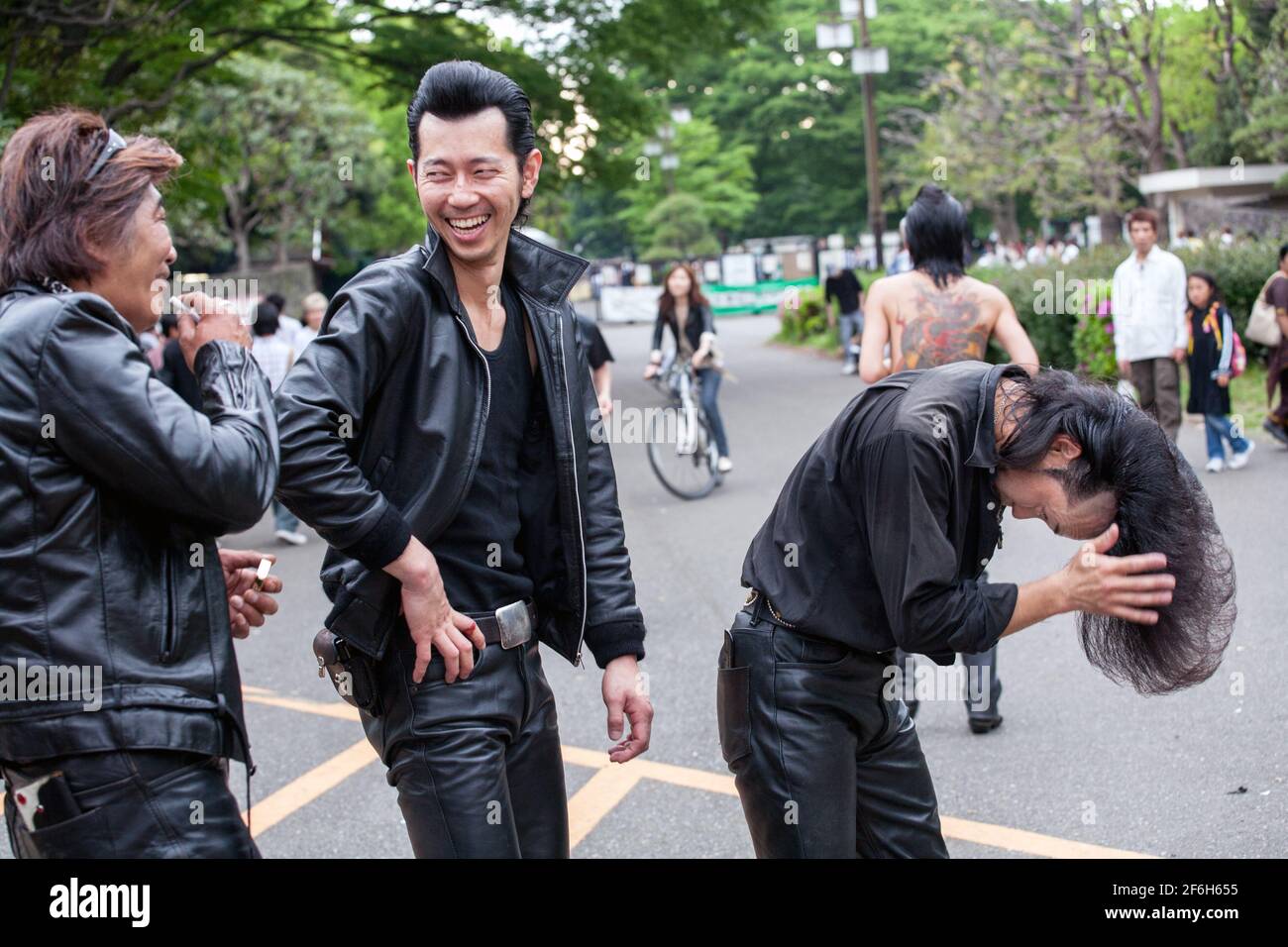 Japanischer Rockabilly in Lederhosen neigt zu seinem riesigen Quiff/Pompadour, während seine Kumpels einen Witz teilen, Yoyogi Park, Harajuku, Tokio, Japan Stockfoto