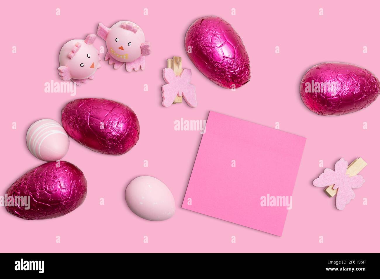 Rosafarbener Osterhintergrund mit Ostereiern, Dekorationen und rosafarbenem unbeschrifttem Papier. Stockfoto