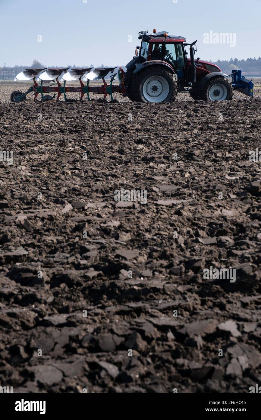 Landwirt im Traktor mit Pflug hinter ihm pflügt durch ein Feld aus