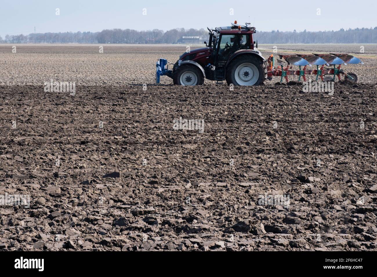 Landwirt im Traktor mit Pflug hinter ihm pflügt durch ein Feld aus