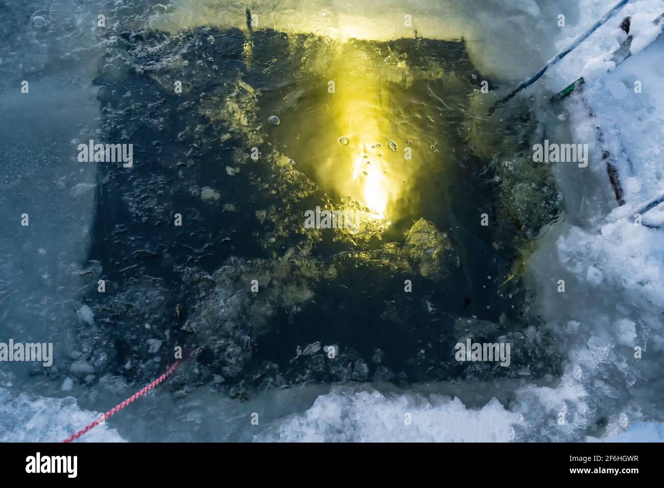 Ein Taucher unter dem Wasser leuchtet mit einer Taschenlampe Fackel einen Eisloch-Eingang mit einem zum Eistauchen Tauchen Stockfoto