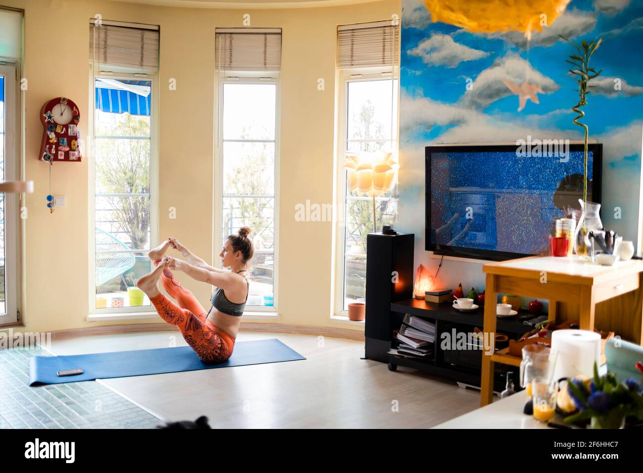 Schöne Frau, die Yoga in aufwärtsgewandter, weit sitzender Pose genießt In ihrer gemütlichen Wohnung Stockfoto