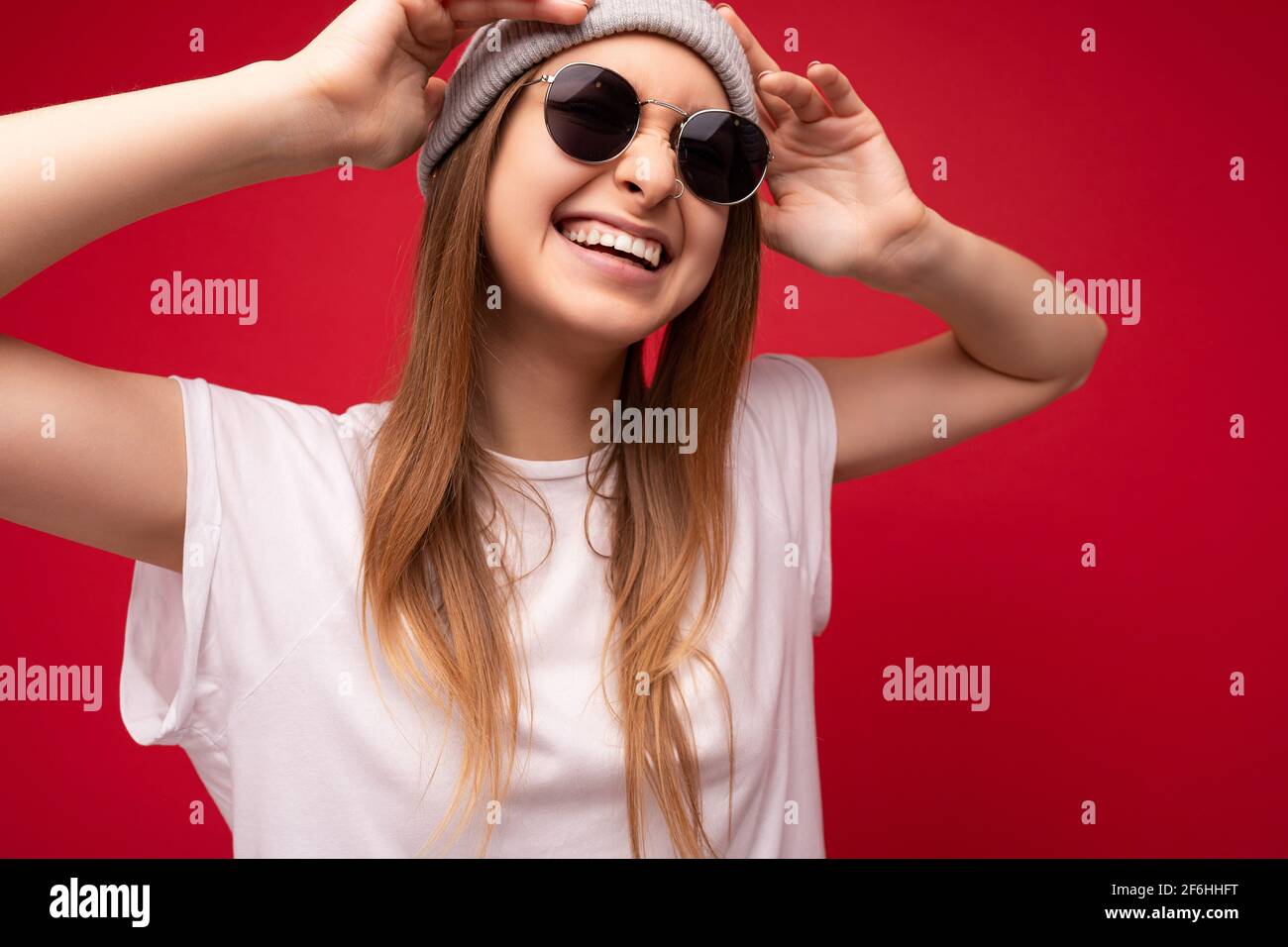 Nahaufnahme von schönen positiv lächelnden jungen dunklen Blondinen Frau trägt legere Kleidung und stilvolle Sonnenbrille isoliert über bunt Stockfoto